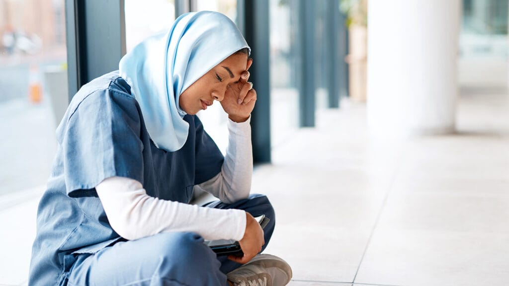 Sad, stress and medical with nurse in hospital with depression, burnout and mental health. Healthcare, anxiety and medicine with muslim woman on the floor of clinic with headache, thinking and tired
