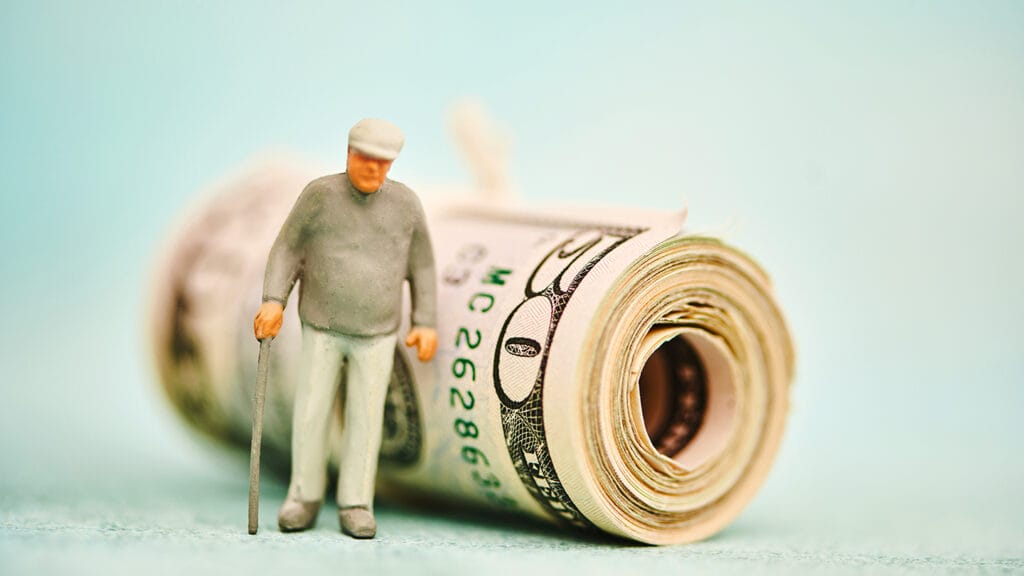 Miniature figure of elderly man with walking stick next to a wad of fifty dollar bills