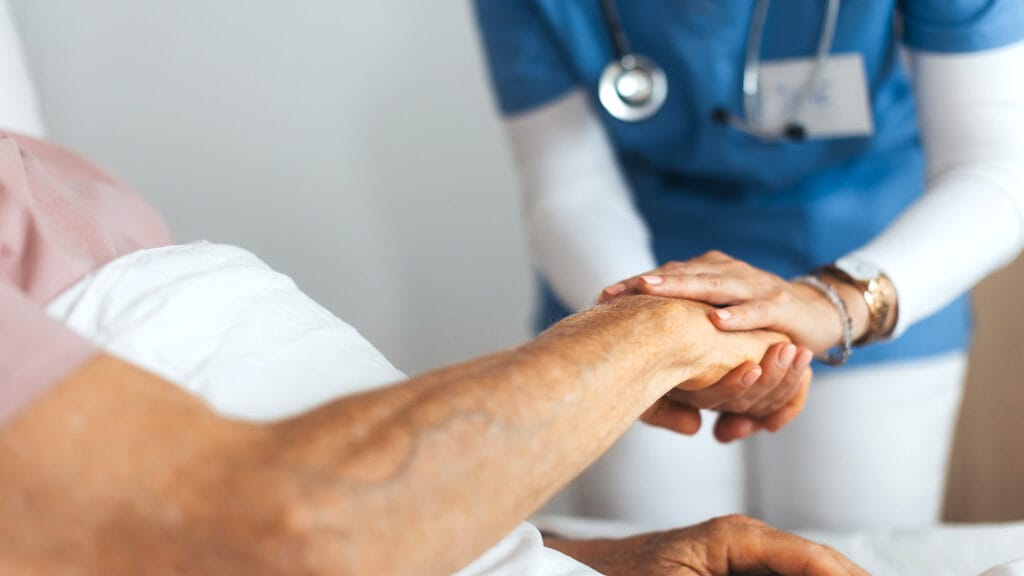 Close-up of caregiver holding senior client hand. Support from nurse to patient, taking care of elderly man in hospital. Emotional support and care in healthcare, hospice care.
