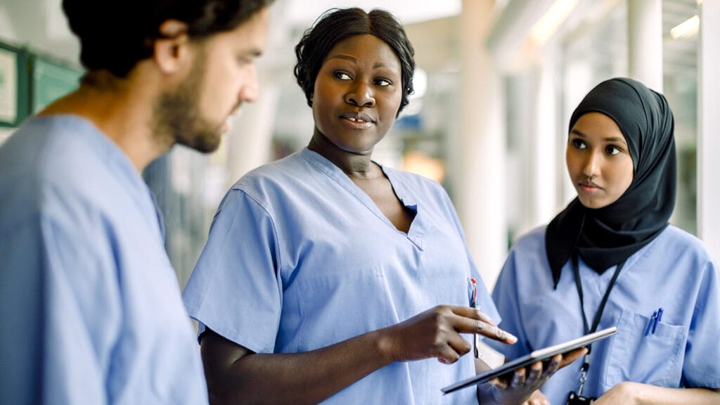 Female nurse with digital tablet talking to colleagues in hospital